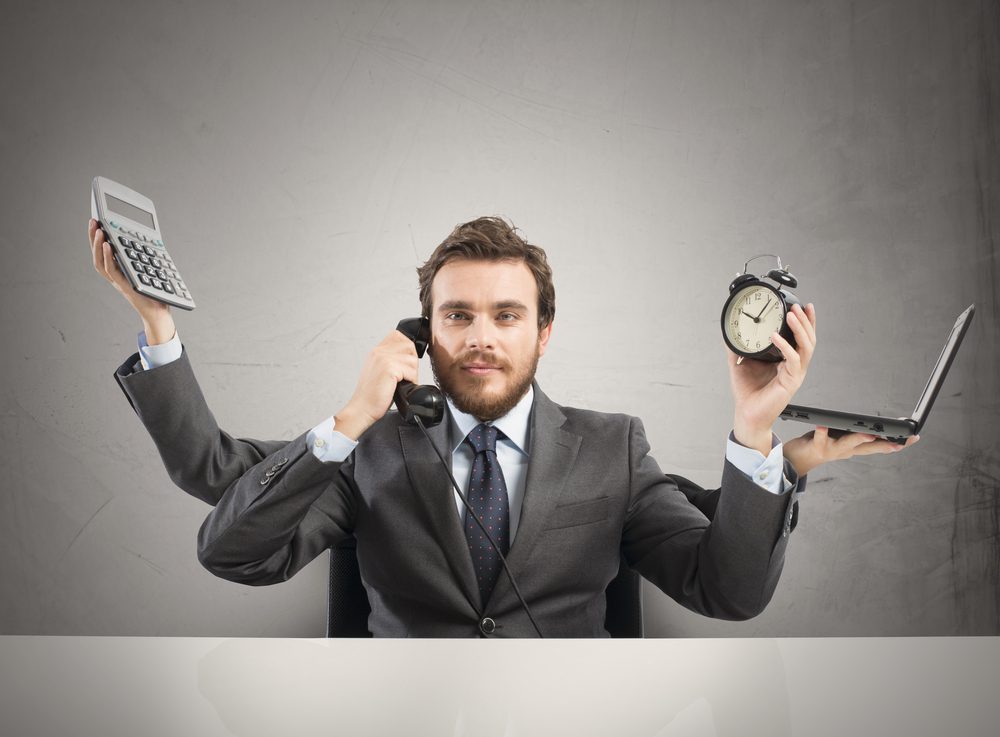 Time management | Person with multiple arms holding a calculator, phone, alarm clock and laptop.