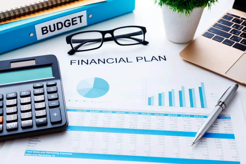 Financial management | graphs and statistics on paper with 'financial plan' written on it. Glasses, calculator and pen present too with a binder with 'budget' written on it.