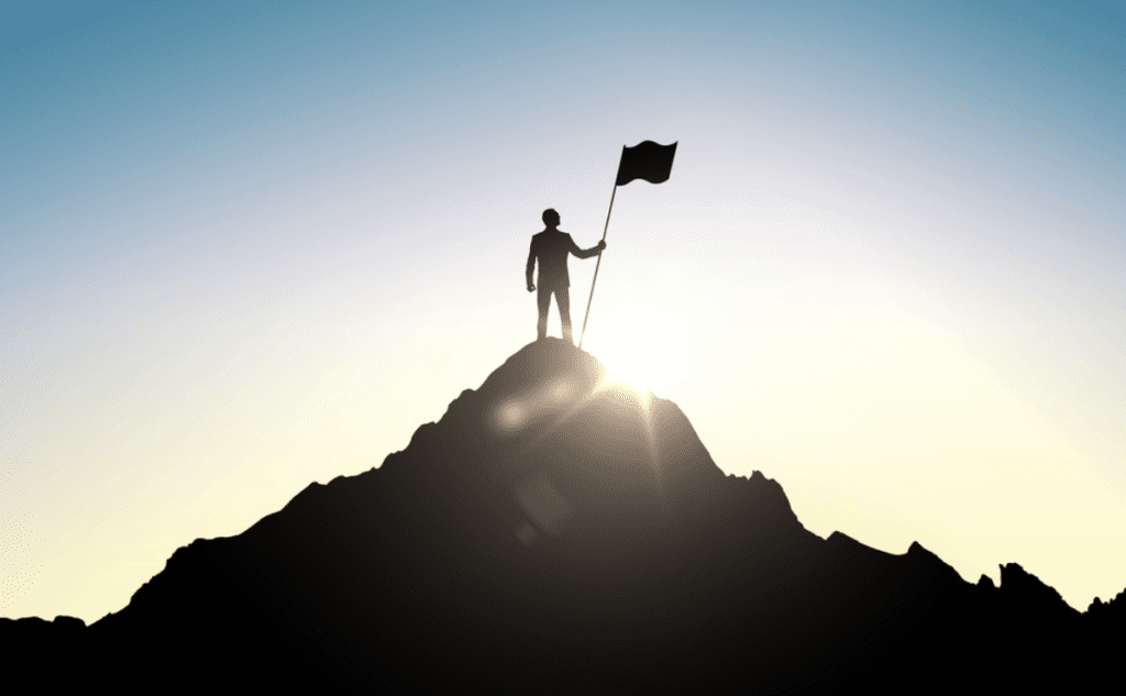 Leadership vs management | person standing on top of mountain in silhouette holding a flag