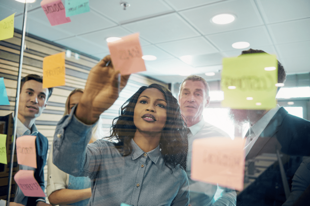 Leadership vs management | People in office sticking post-it notes on glass wall. 