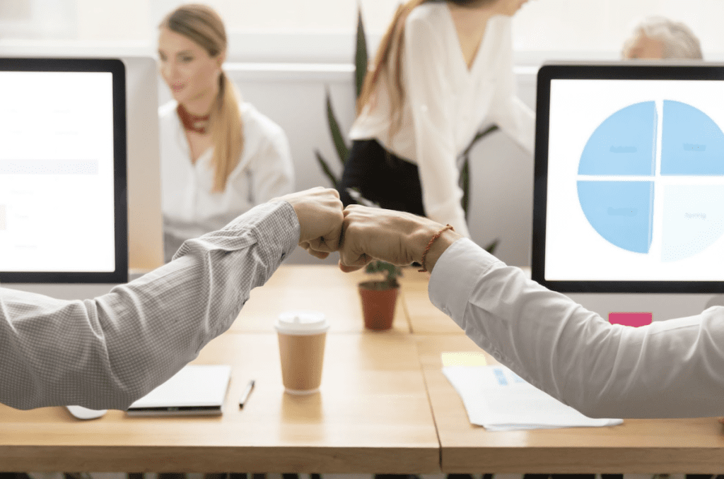 Company culture | Two people fist-bumping in an office.