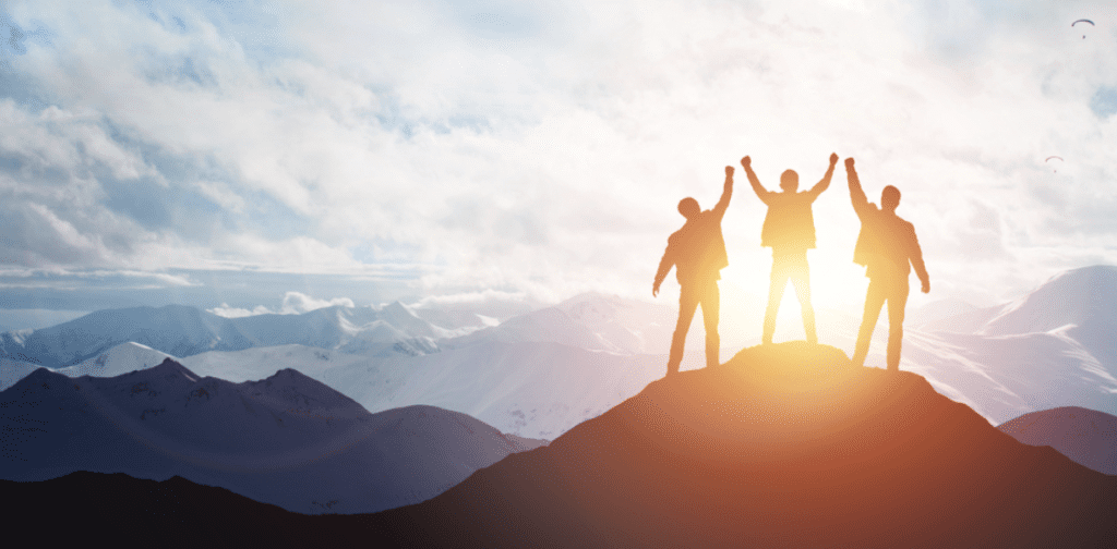 People-oriented leadership | Group standing on summit of a mountain with sunset and glider in background.