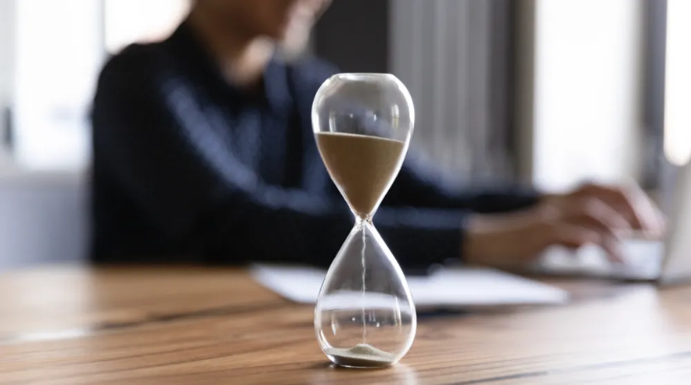 Time management techniques | Person using desk with an hourglass filled with sand in front.