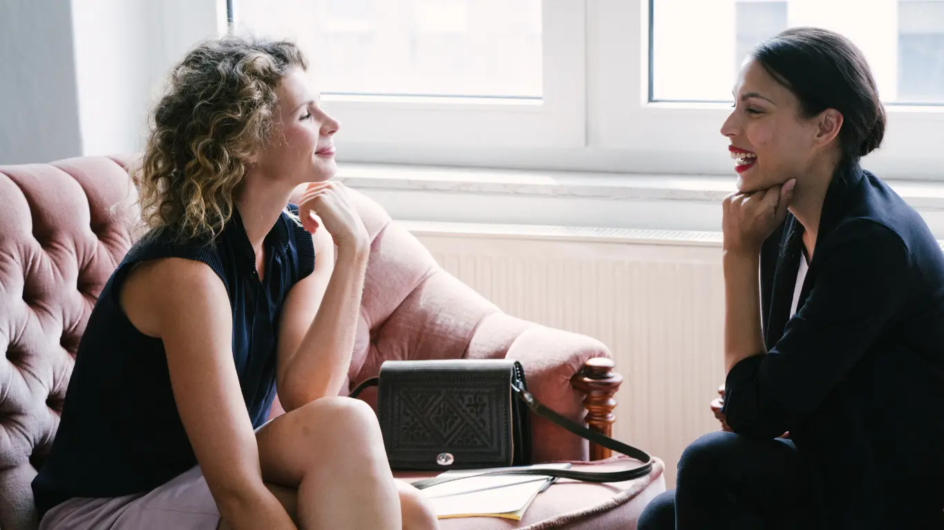 2 females sat on a sofa talking and smiling