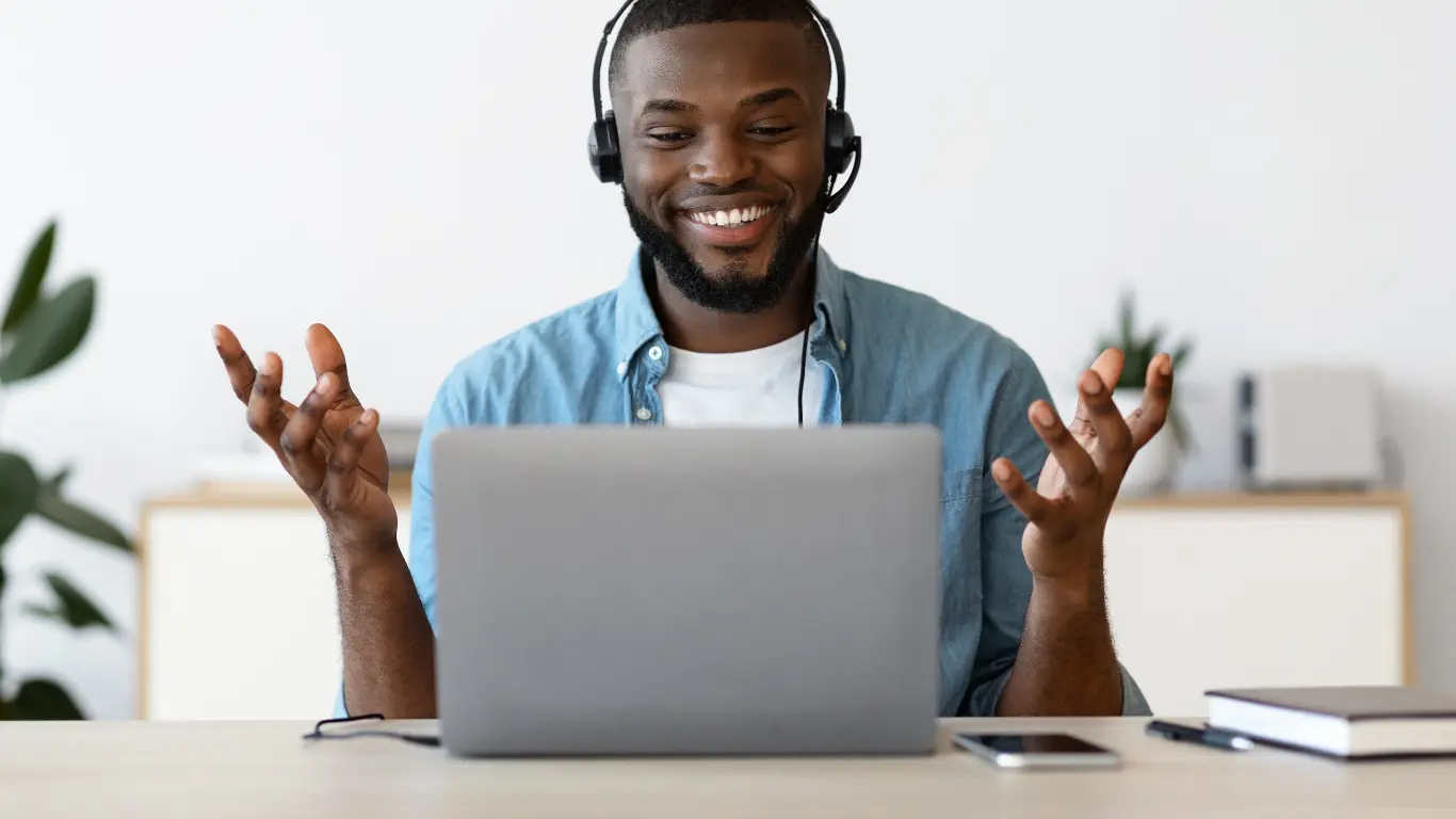 smiling male sat in front of a laptop asking the right questions to find a business coach near me