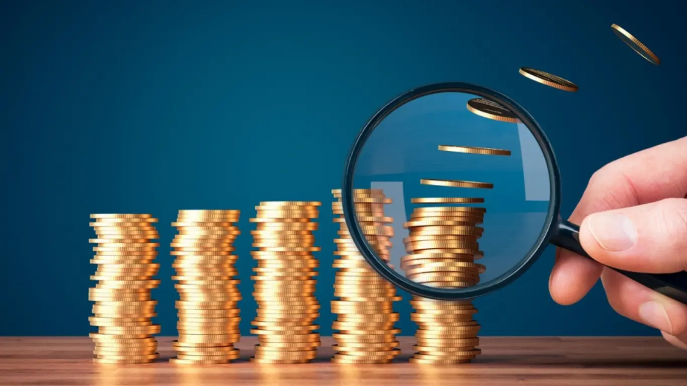 piles of gold coins with a magnifying glass