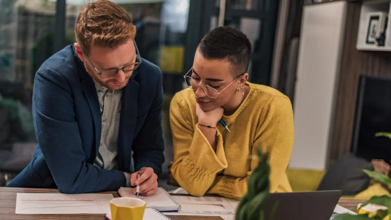 a male and a female looking at a notebook and writing about is a business coach worth it