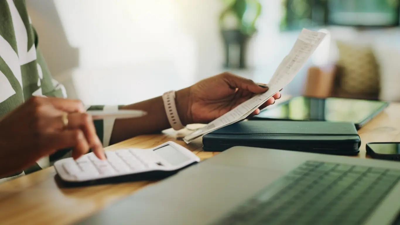 person at a desk, holding paper and using a calculator